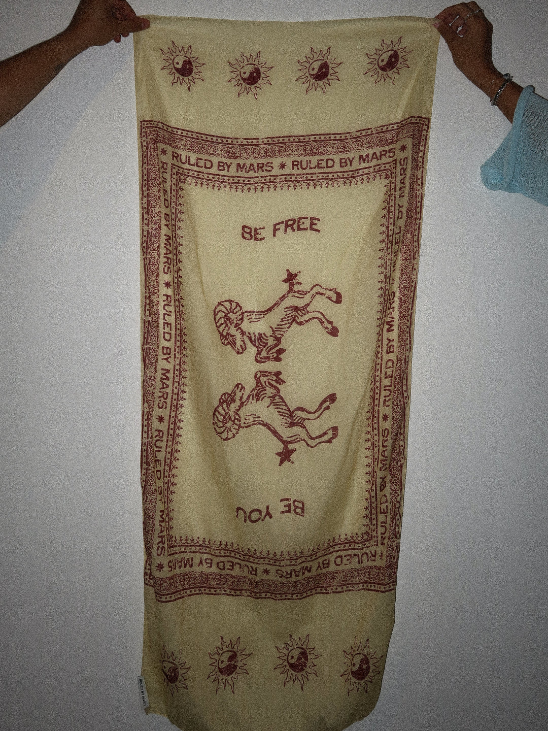 Yellow fabric with red text and symbols, held by two hands against a plain background