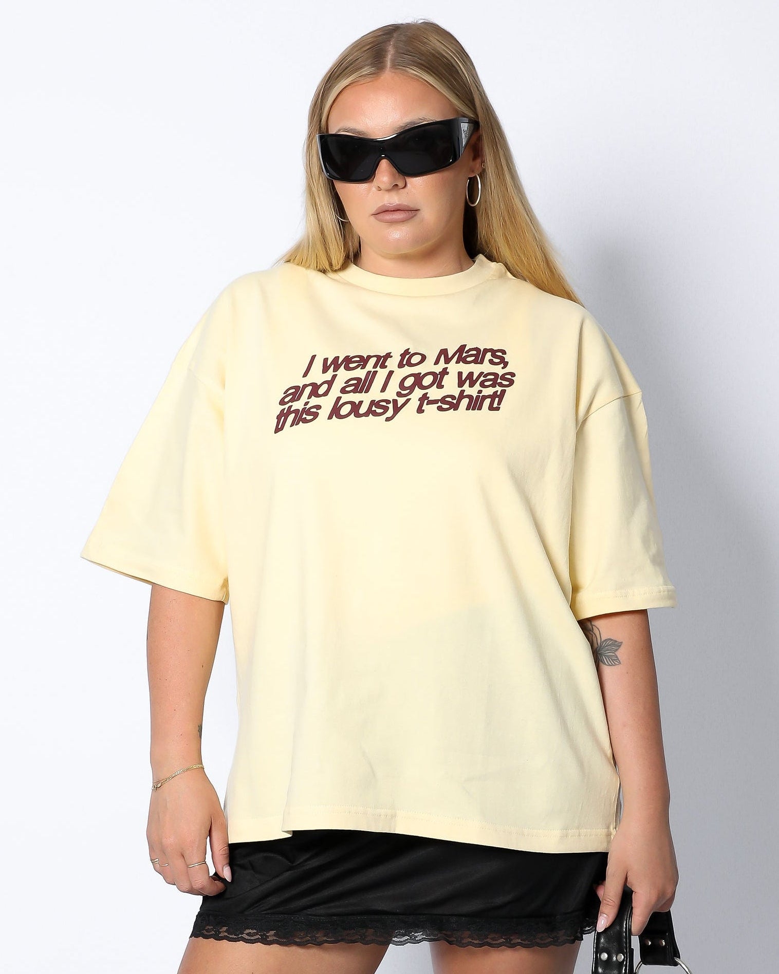 Person wearing a light yellow t-shirt with text and black shorts on a white background