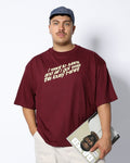 Person wearing a maroon t-shirt with text, holding a magazine against a white background