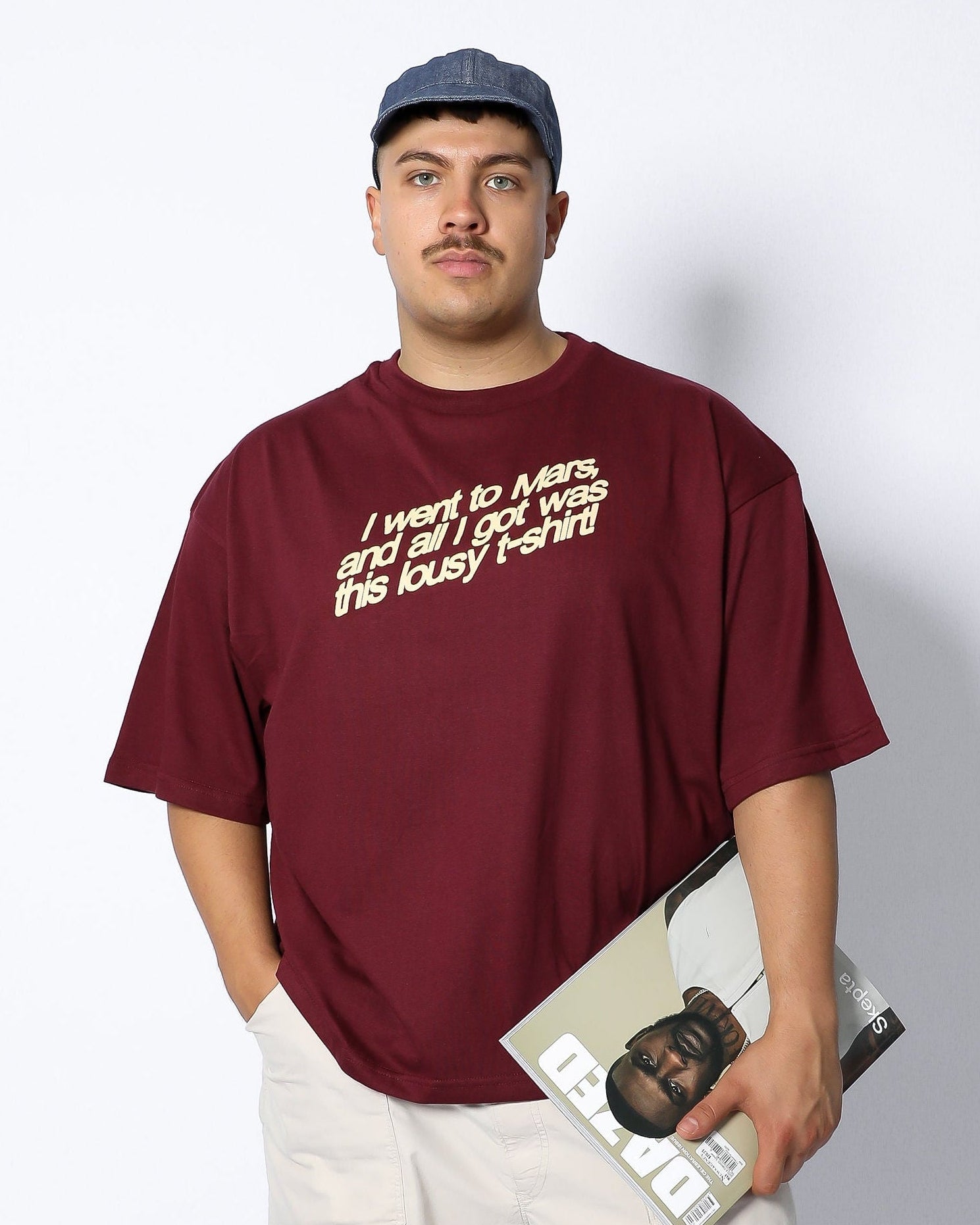 Person wearing a maroon t-shirt with text, holding a magazine against a white background