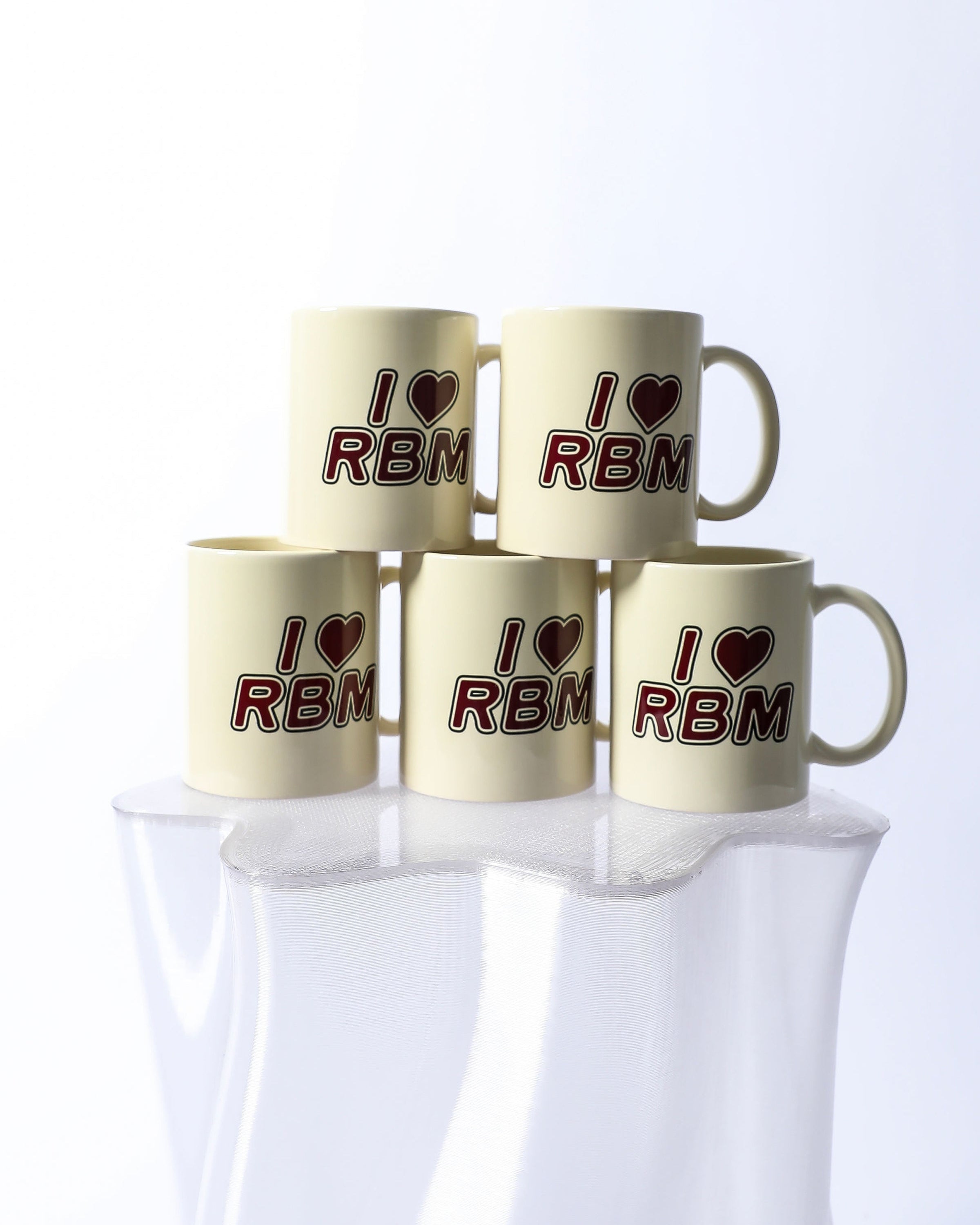 Five beige mugs with 'I ❤️ RBM' text on a white background