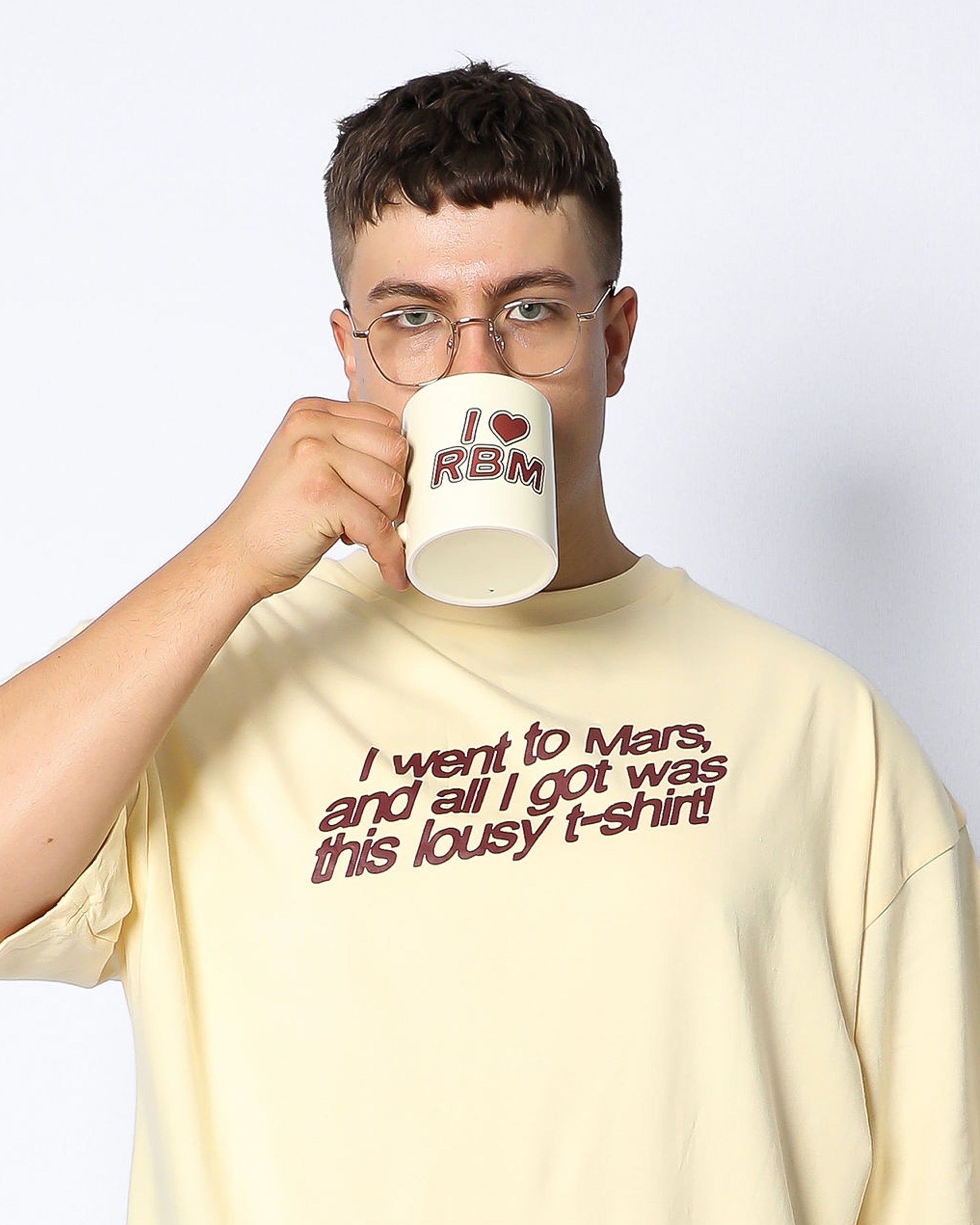 Person wearing a yellow t-shirt with text and holding a mug with 'I ❤️ RBM' text.